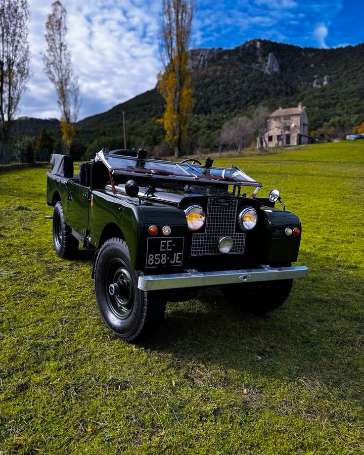 an old black truck parked on top of a lush green field with mountains in the background