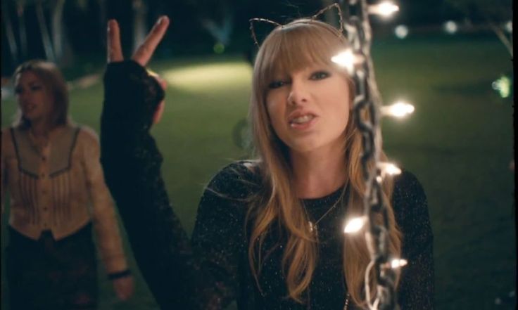 a woman standing in the grass with her hand up and lights strung all around her