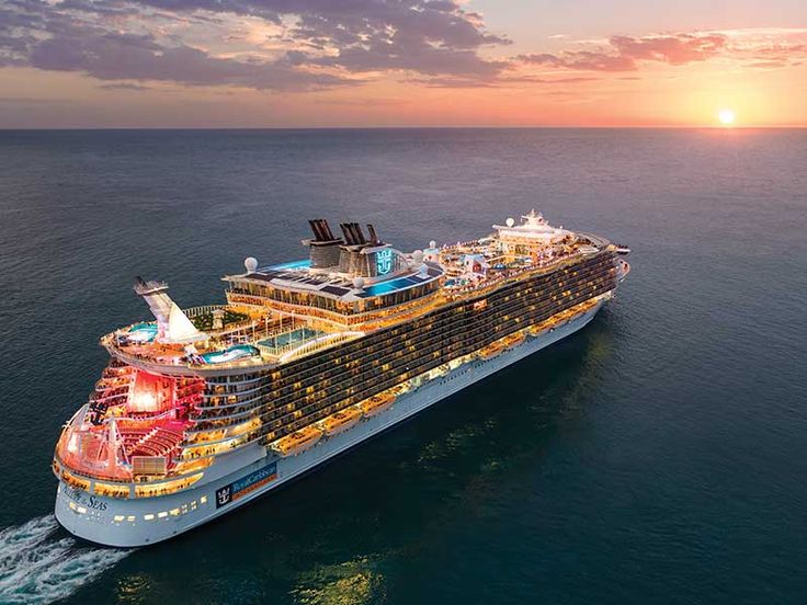 a large cruise ship in the middle of the ocean at sunset with its lights on