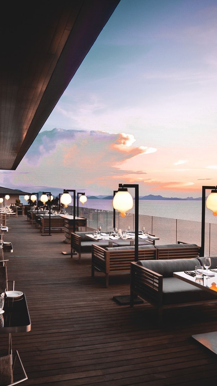 an outdoor dining area overlooking the ocean at sunset or dawn with wooden tables and benches