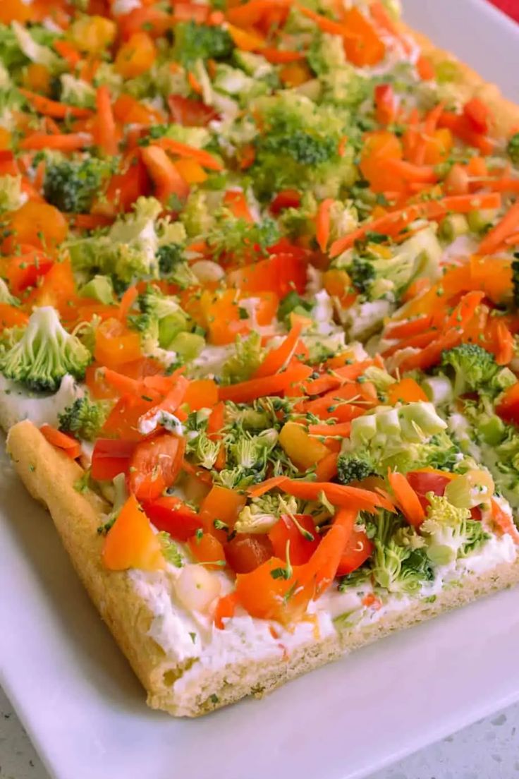 a square pizza topped with broccoli, carrots and other toppings on a white plate