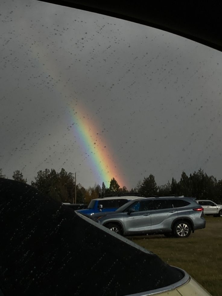 a rainbow is seen in the sky over some parked cars on a cloudy day with raindrops