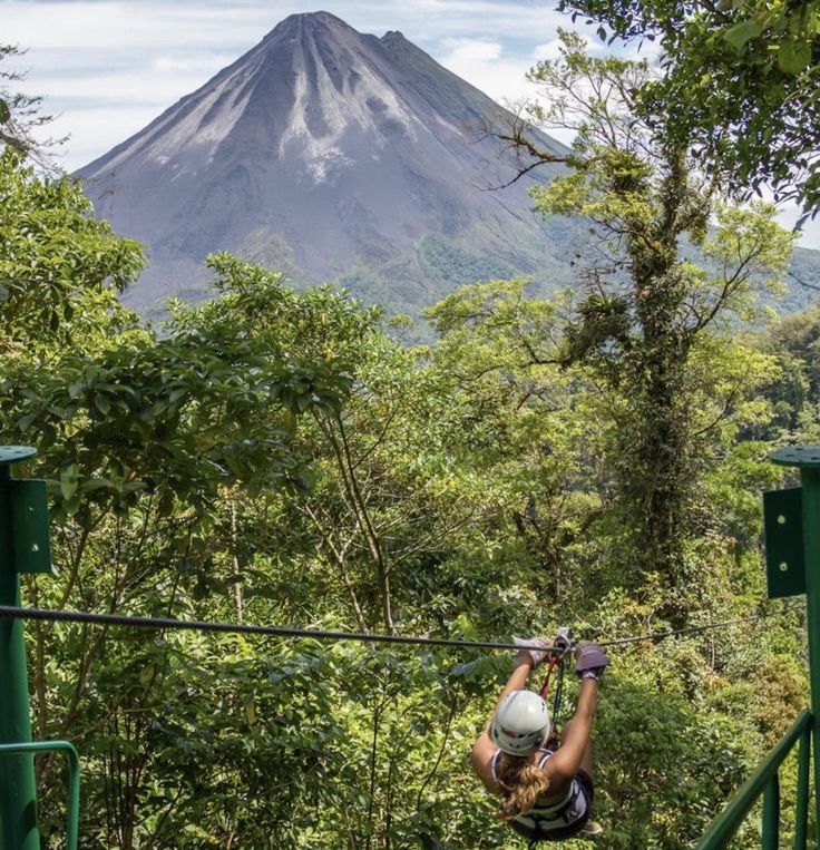 a woman zips through the trees in front of a mountain with a helmet on