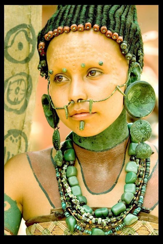 a woman with green makeup and necklaces on her face, wearing beads around her neck