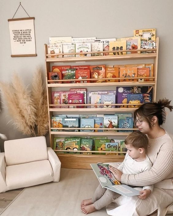 a woman sitting on the floor reading to a child in front of a bookshelf