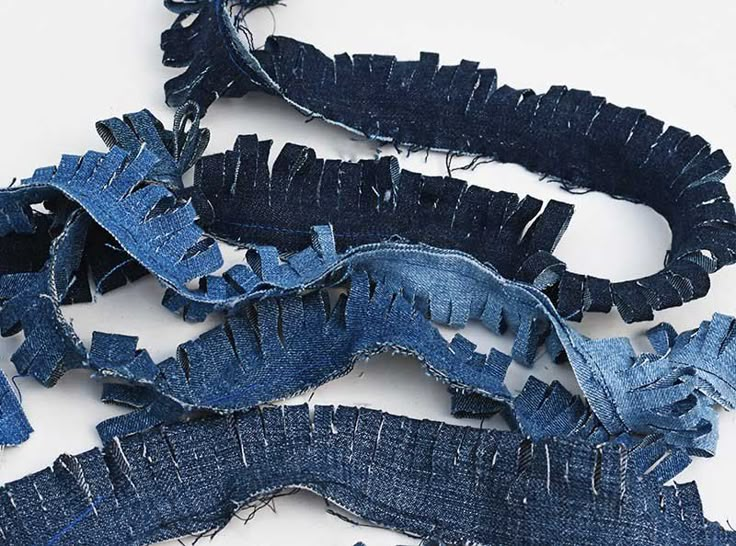 several pieces of blue jeans with holes cut in half on a white surface, including one torn off and the other ripped