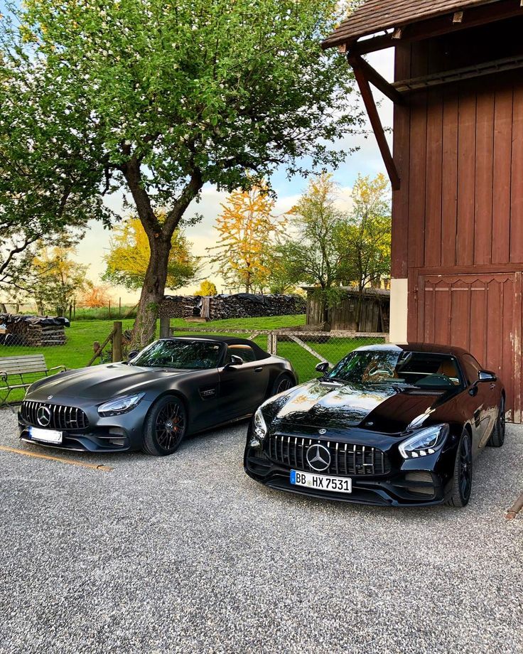 two black sports cars parked next to each other in front of a barn with trees