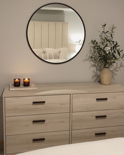 a dresser with candles and a round mirror above it