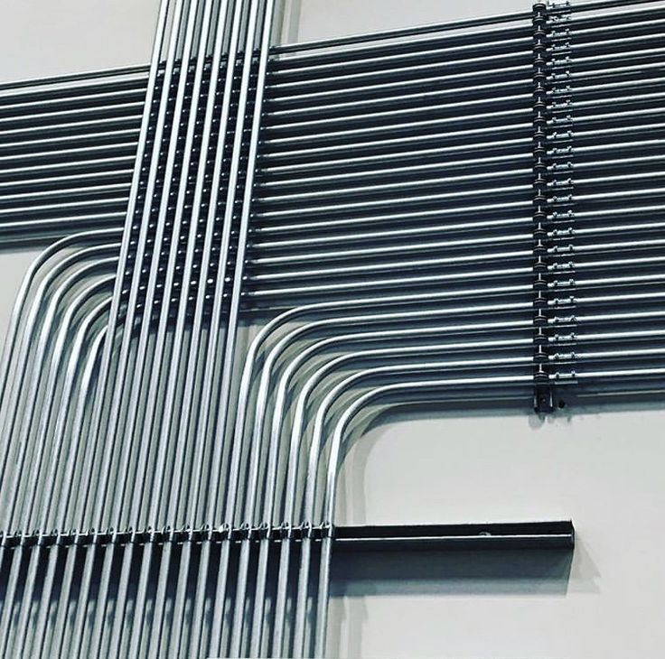 an abstract sculpture made out of metal tubes and rods on a wall with a clock in the middle