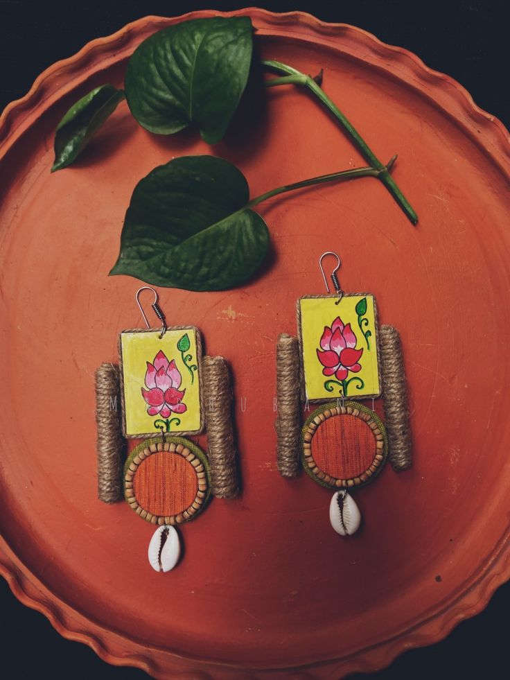 two wooden earrings with flowers on them sitting on a plate next to a green leaf