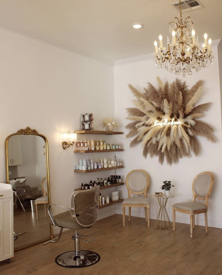 In a boho salon setting, a beige salon styling chair stands in front of a large mirror. Hair Salon Shampoo Area Decor, Pretty Hair Salon Interior, Boho Salon Inspiration, White And Gold Salon Suite, Vintage Salon Chair, Calming Salon Decor, Green Accent Wall Salon, Beauty Salon Accent Wall Ideas, Backdrop For Salon