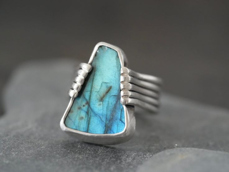 This one of a kind labradorite statement ring was handmade by me in my studio. A gorgeous, deep teal blue labradorite with excellent shiller, raw cut with a natural shape and polished surface, is the focal element of this piece. The stone is set in fine silver and held in place by a unique, handcrafted sterling silver band. It is an incredible stone in a unique piece, I initially wanted to keep it for myself but I am now happy to present it here. As most mazulou items this ring is one of a kind. Measurements: ring size 6.5 stone: 20x15mm band: 7.4 x1.mm Hand Forged Labradorite Blue Jewelry, Hand Forged Blue Labradorite Jewelry, Unique Blue Labradorite Ring, Unique Labradorite Ring With Large Stone, Unique Labradorite Rings With Natural Stones, Blue Labradorite, Deep Teal, Natural Shapes, Sterling Silver Bands