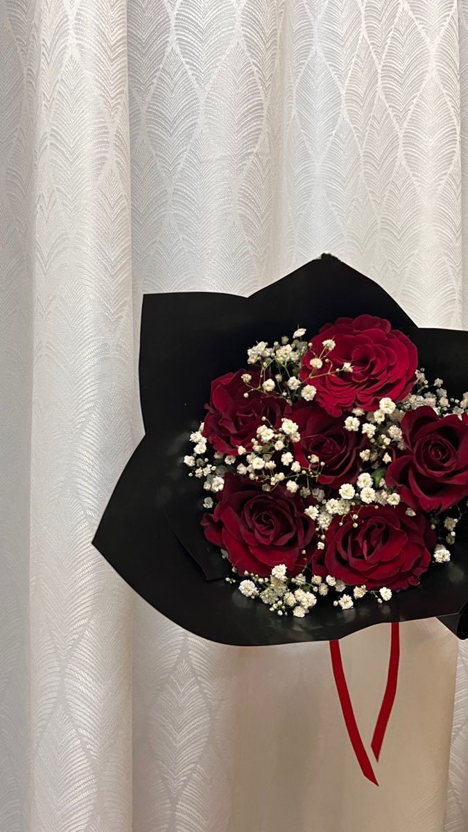 a bouquet of red roses in a black paper wrapper with baby's breath