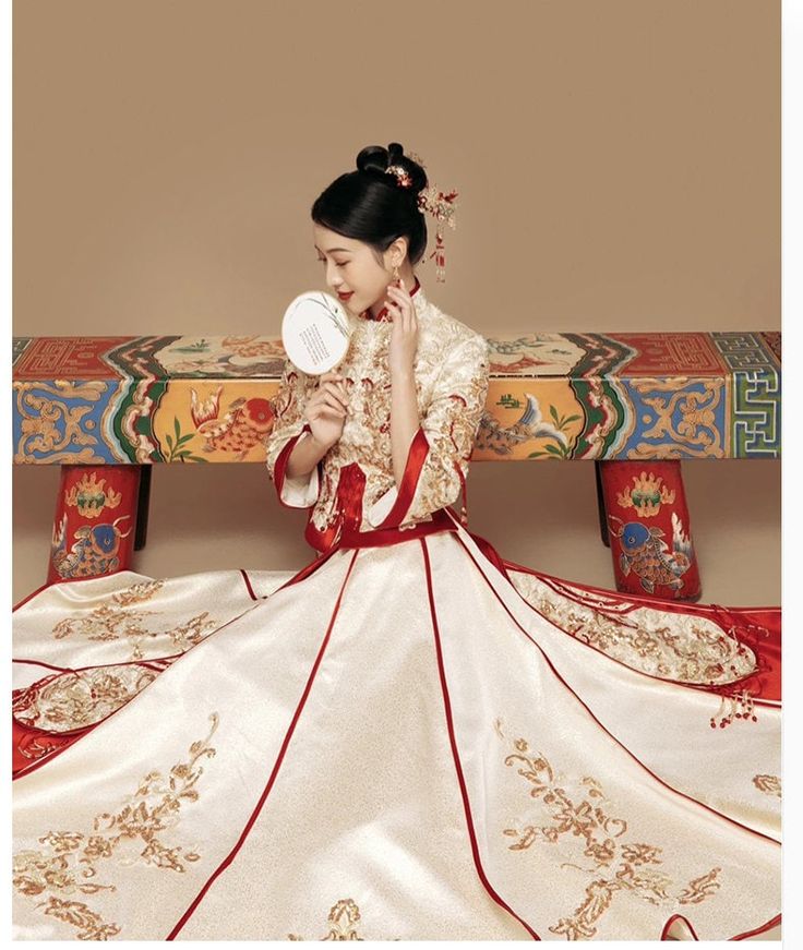 a woman sitting on top of a bench wearing a dress and holding a mirror in her hand