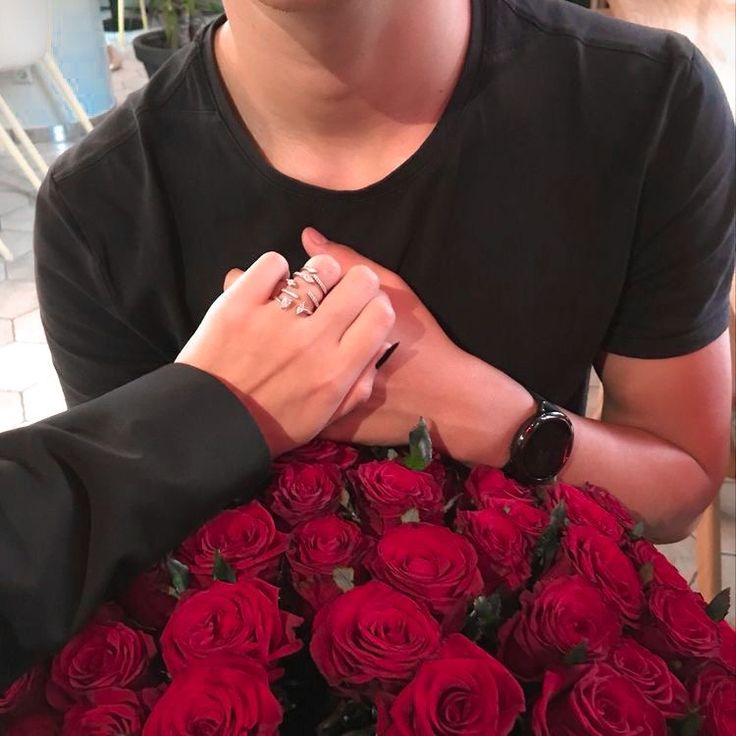 two people holding hands over a bouquet of red roses