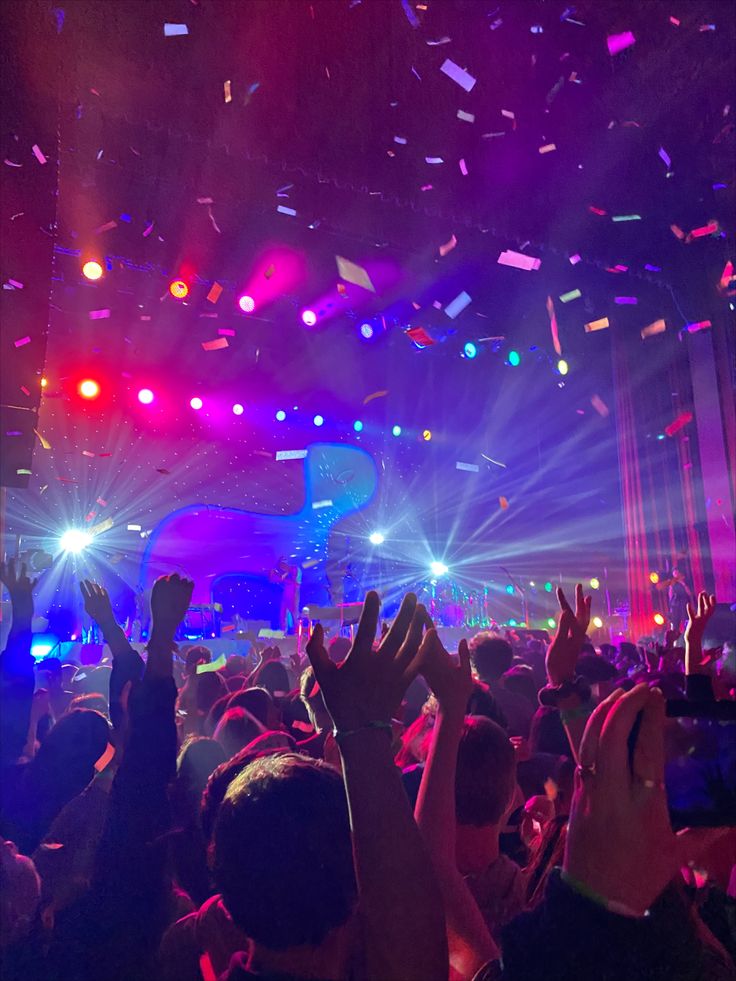 a crowd at a concert with confetti falling from the ceiling and people raising their hands in the air