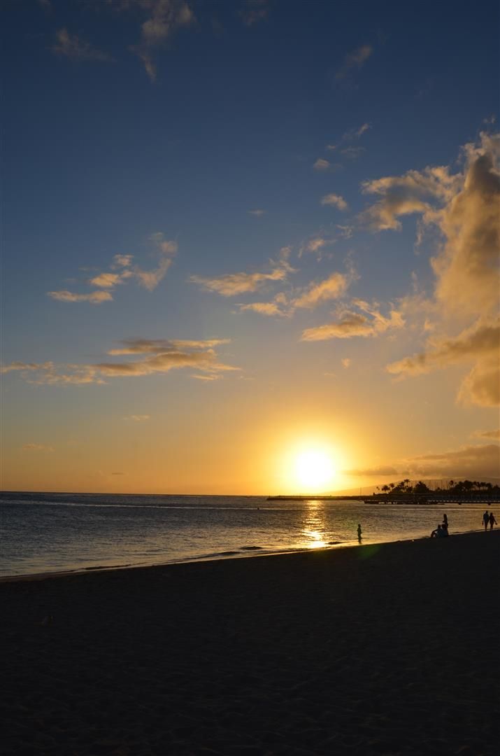 the sun is setting over the ocean with people on the beach