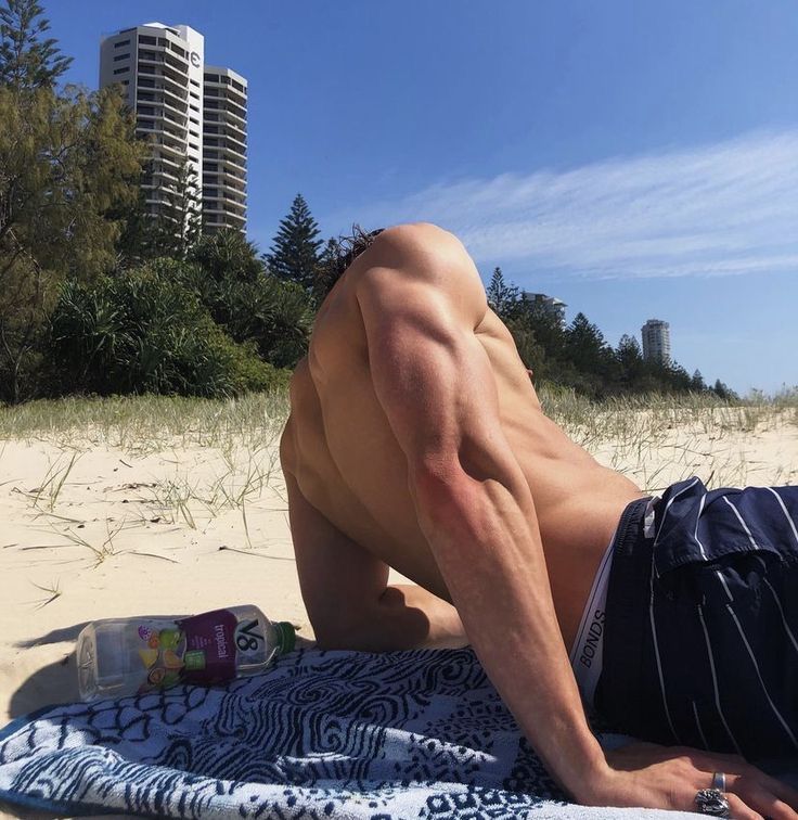 a shirtless man laying on top of a beach next to a blue and white towel