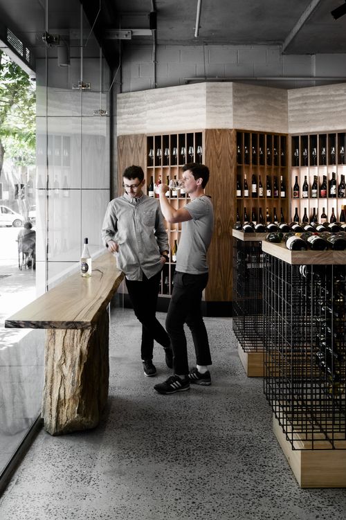 two men standing in front of a counter filled with wine bottles