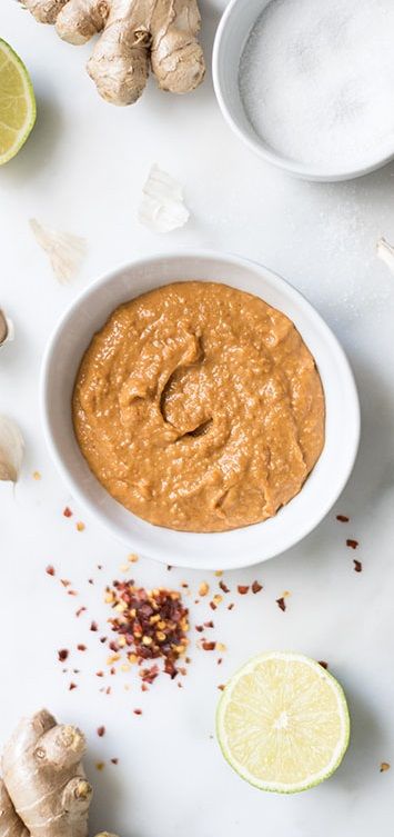 a white bowl filled with peanut sauce next to sliced ginger and limes