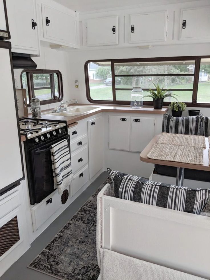 an rv kitchen with white cabinets and black stove top oven next to a dining table