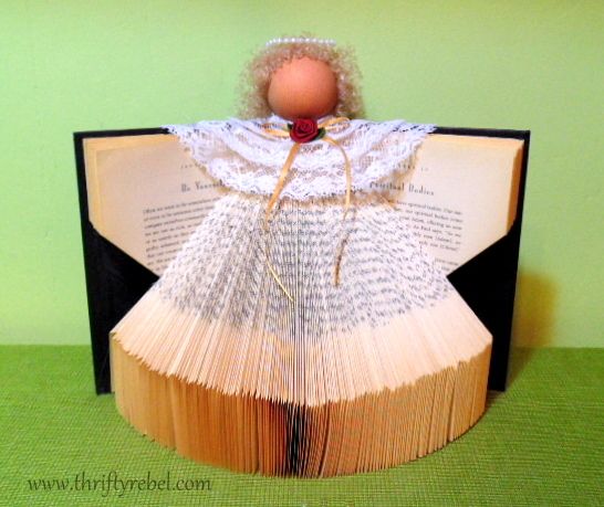 an open book with a doll sitting on top of it and the pages are folded