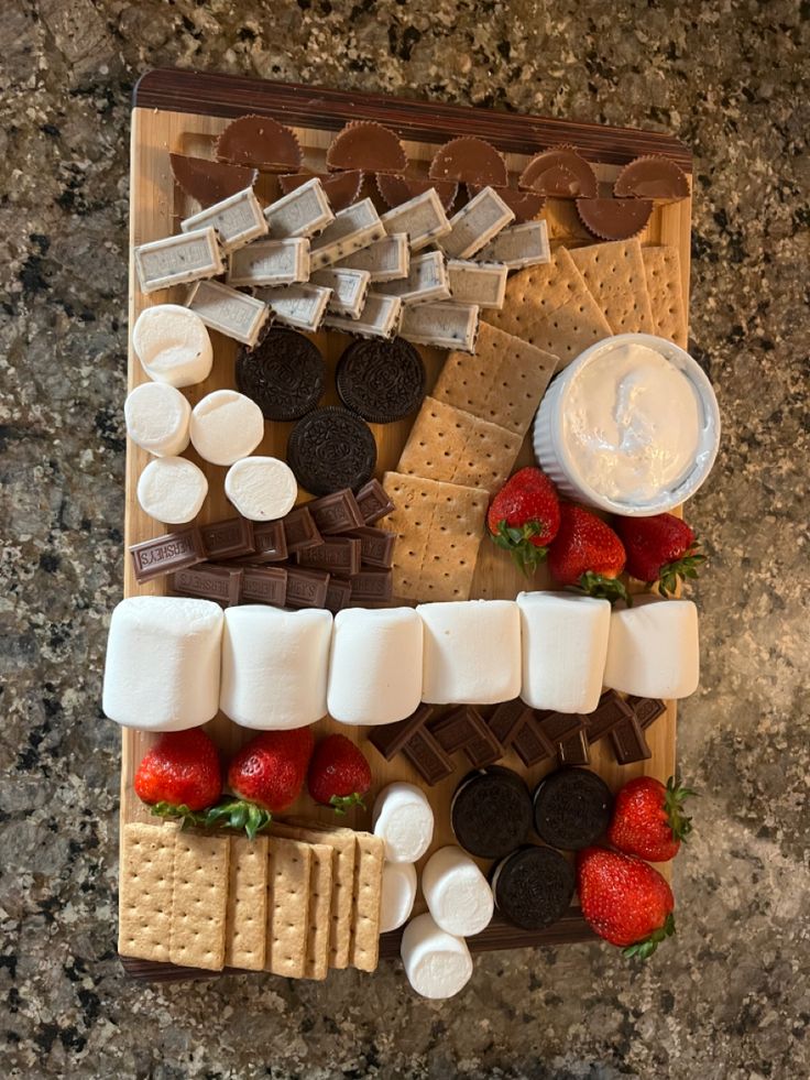 an assortment of desserts arranged on a board with chocolate, marshmallows and strawberries