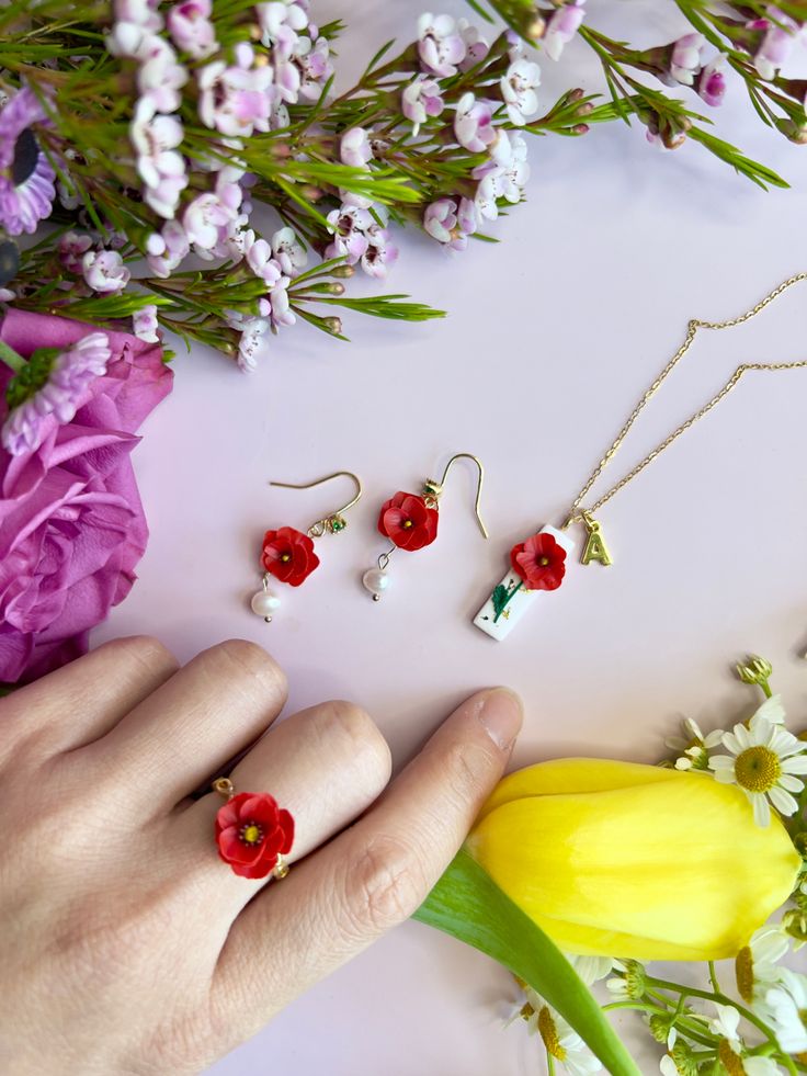 a person's hand with three red and white flowers on it next to some jewelry