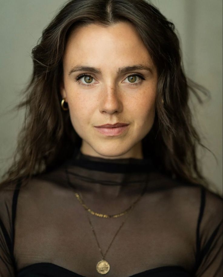 a woman with long hair wearing a black top and gold necklaces is looking at the camera