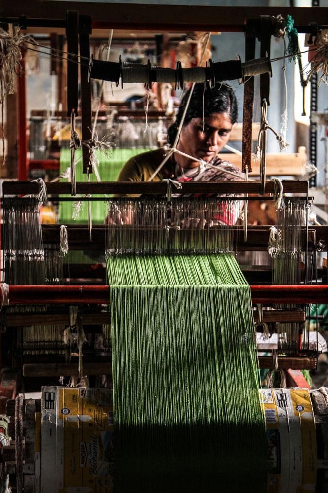 a man working on a weaving machine with green yarn hanging from it's sides