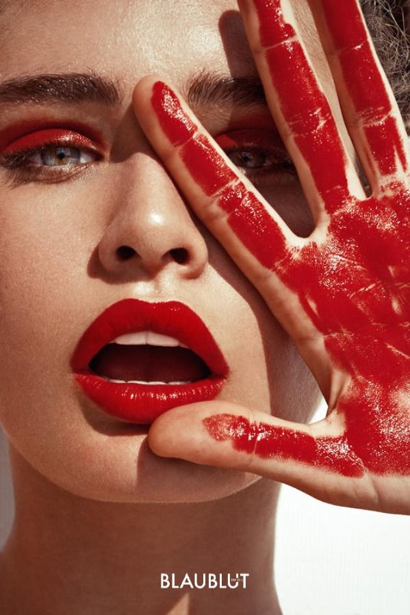 a woman with red makeup holding her hand up to her face