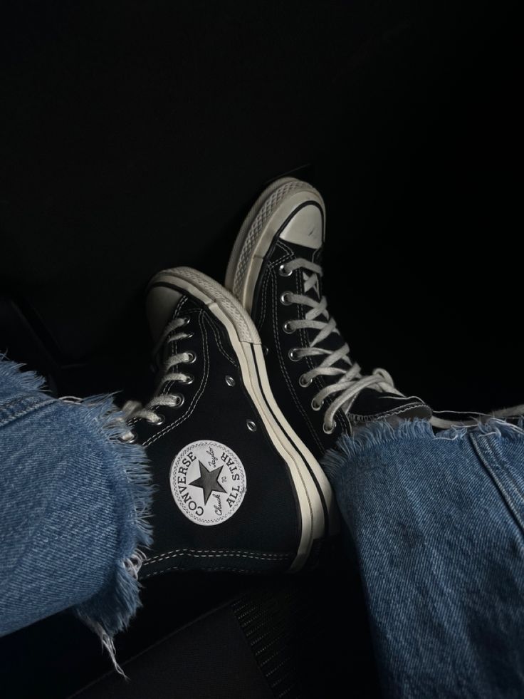 a pair of black and white converse shoes sitting on someone's legs in jeans