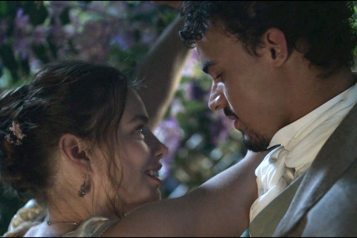 a man and woman standing next to each other with flowers in the backgrund