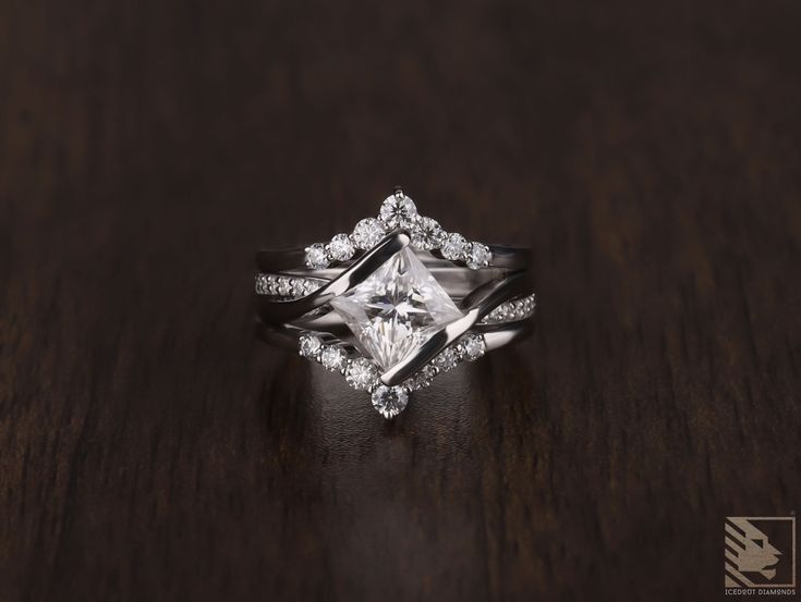 an engagement ring with a princess cut diamond surrounded by round brilliant diamonds on a wooden surface