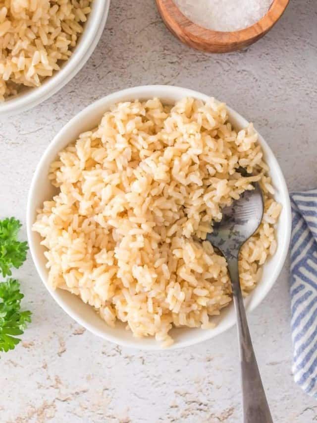 two bowls filled with rice and parsley on top of a white countertop next to a wooden spoon