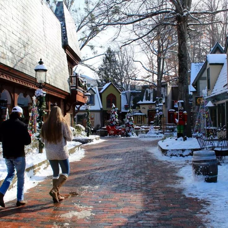 two people walking down a brick road in the snow near shops and christmas decorations on display