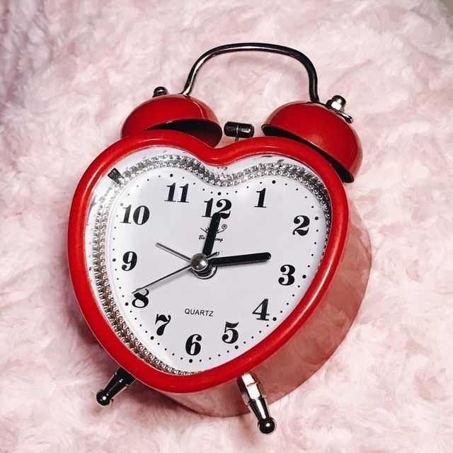 a red alarm clock sitting on top of a pink blanket