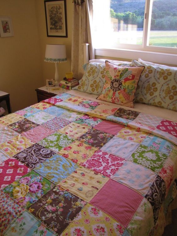 a bedroom with a bed covered in colorful patchwork quilts and pillows, next to a window