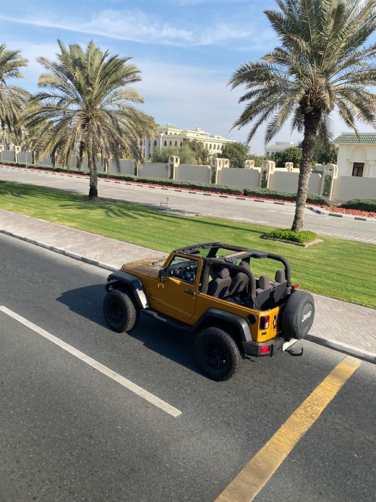 a jeep driving down the street with palm trees in the background