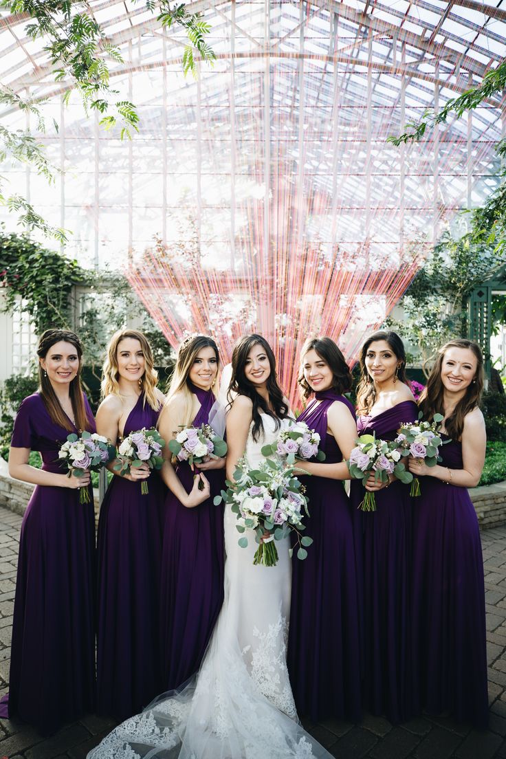 a group of women standing next to each other in front of a glass structure holding bouquets