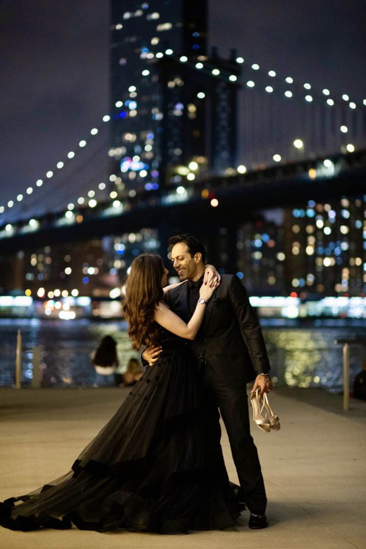 a man and woman standing next to each other in front of a bridge at night