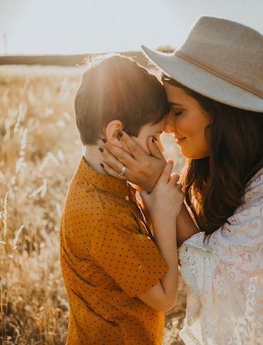 a woman hugging a boy in a field with the sun shining on her and he is wearing a hat