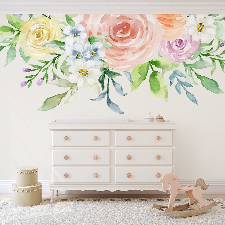 a white dresser sitting next to a wall with flowers painted on the top and bottom