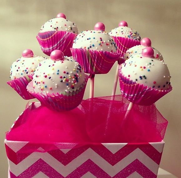 pink and white cupcakes with sprinkles on them in a box