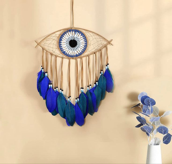 a blue and white dream catcher hanging on the wall next to a vase with flowers