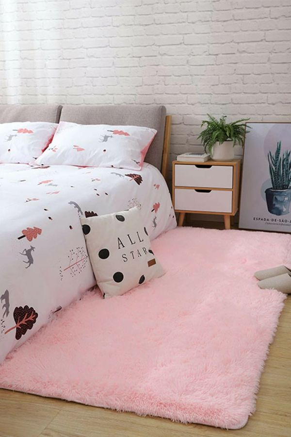 a bedroom with a pink rug and white bedding on the floor next to a brick wall