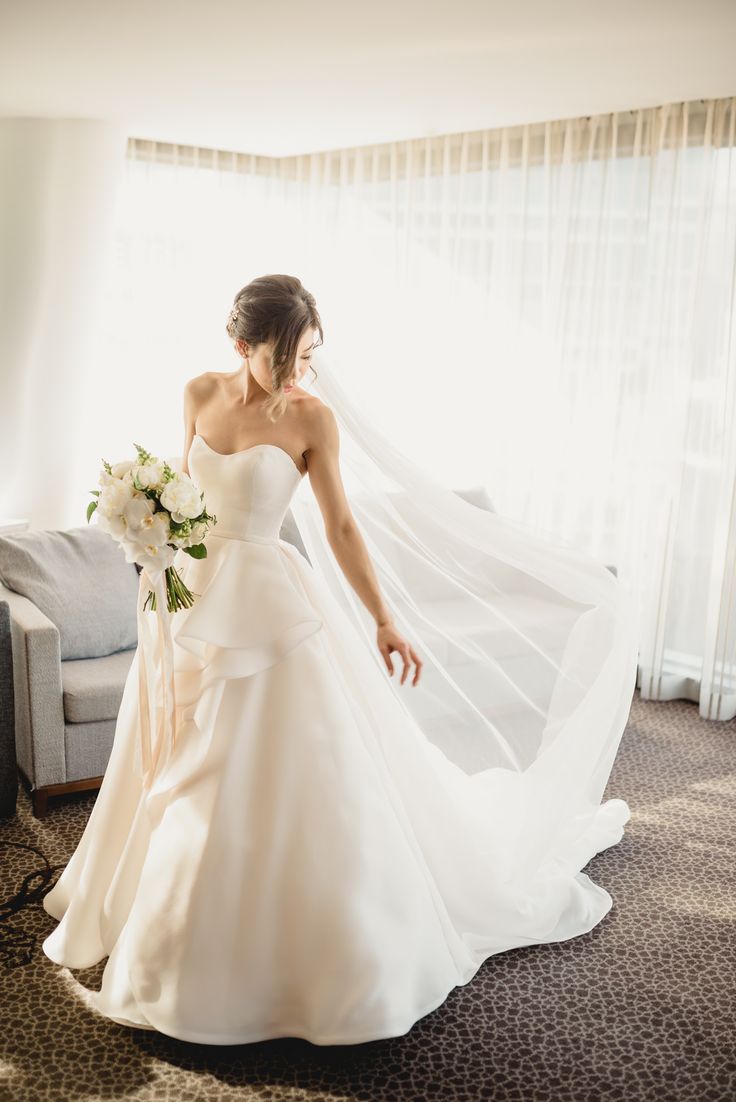 a woman in a wedding dress is walking through the room with her veil over her head