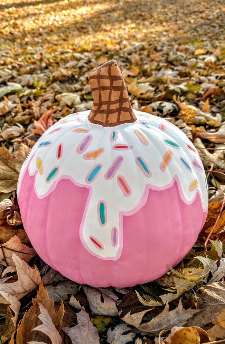 a pink pumpkin with sprinkles and a cone on top sitting in leaves