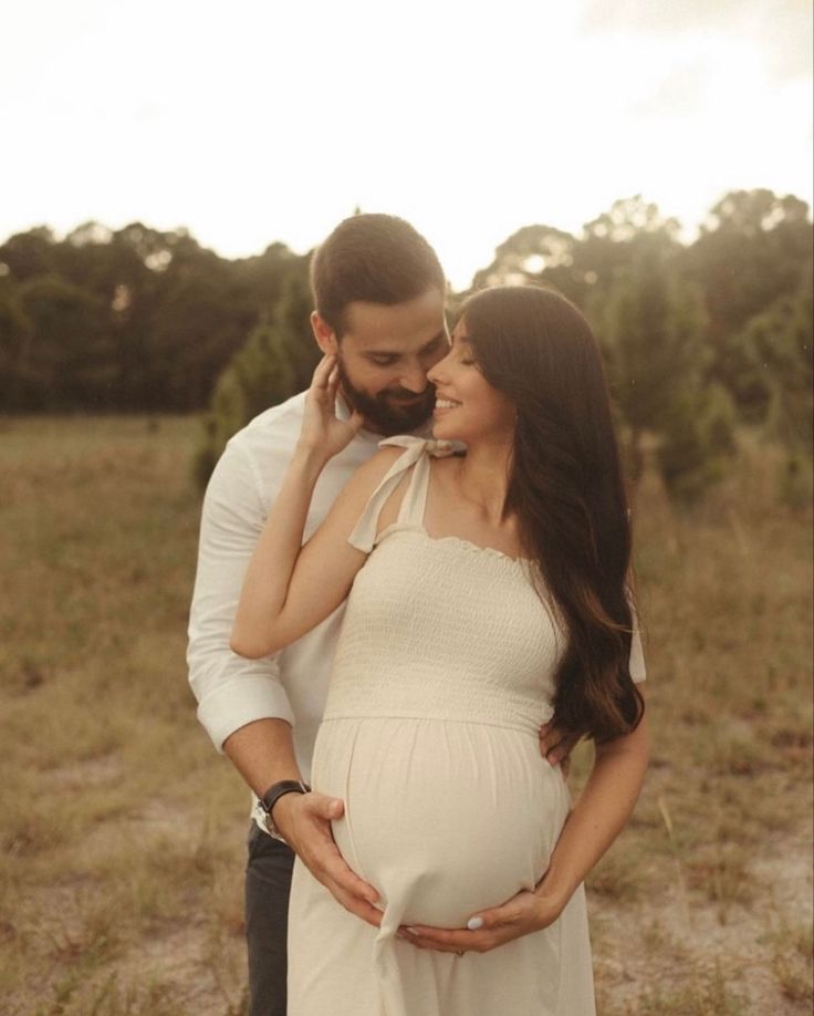 a pregnant couple cuddles while standing in a field