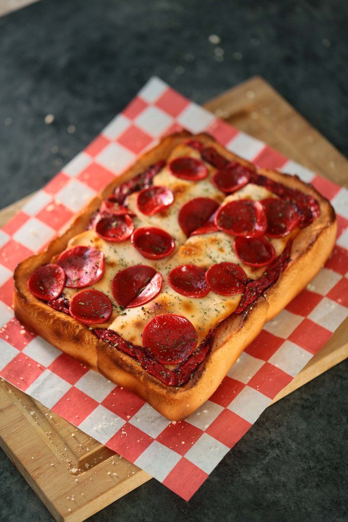 a square pizza with pepperoni and cheese on a checkered paper towel sitting on top of a wooden cutting board